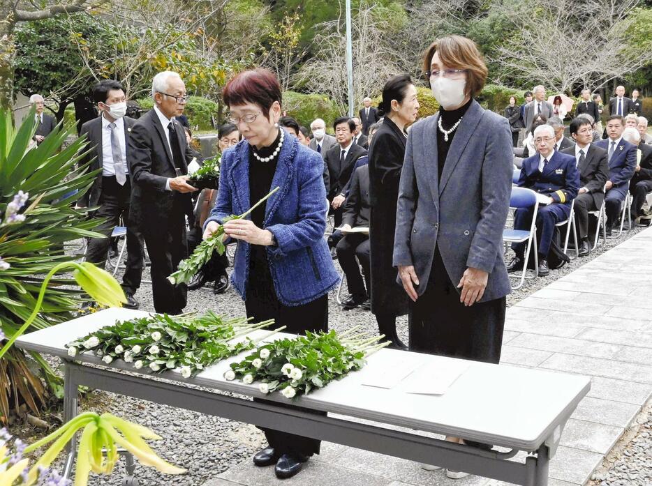 記念碑の前で白菊を供える参列者