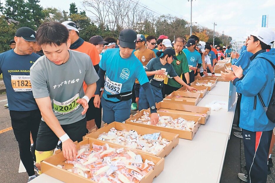 新湊漁協前のエイドステーションでかまぼこを手に取るランナー＝射水市八幡町