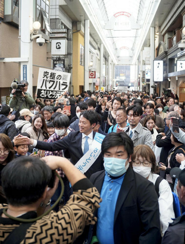 商店街を練り歩く斎藤氏。行く先々で批判するメッセージを掲げる人がいた（１０日、神戸市中央区で）