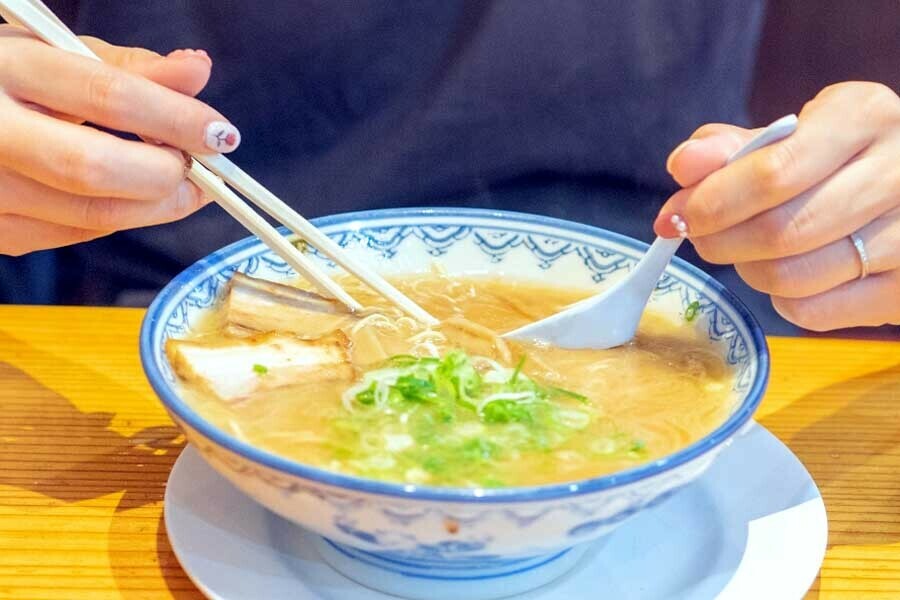 カウンター形式の店舗でラーメンを食べる人（画像：写真AC）