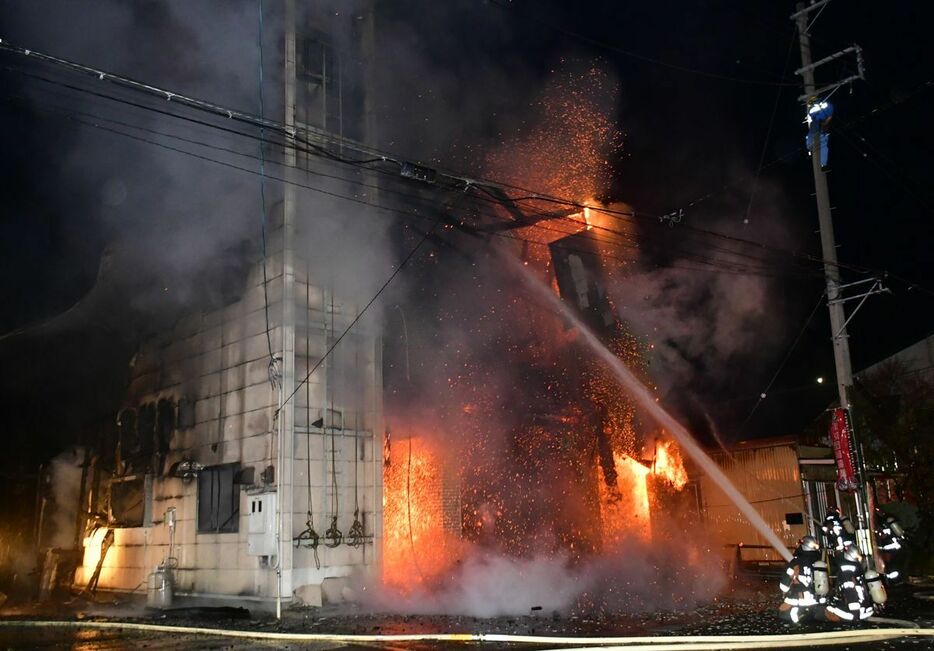 火が上がる屯所に放水する消防隊員＝18日午前4時49分、三沢市三沢猫又