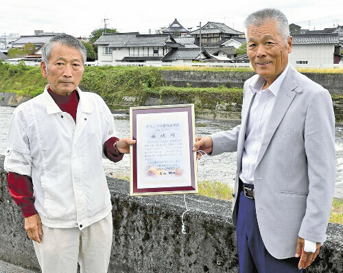 西城川を背にグランプリ証明書を手にする津川組合長（右）と山田放流委員長（広島県庄原市で）