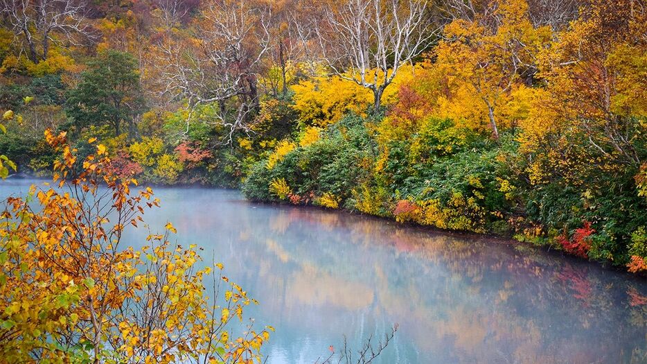 青森市の「地獄沼」で、周囲の紅葉が青い水面に映り込み、鮮やかなコントラストを見せている（2024年10月16日撮影、時事）