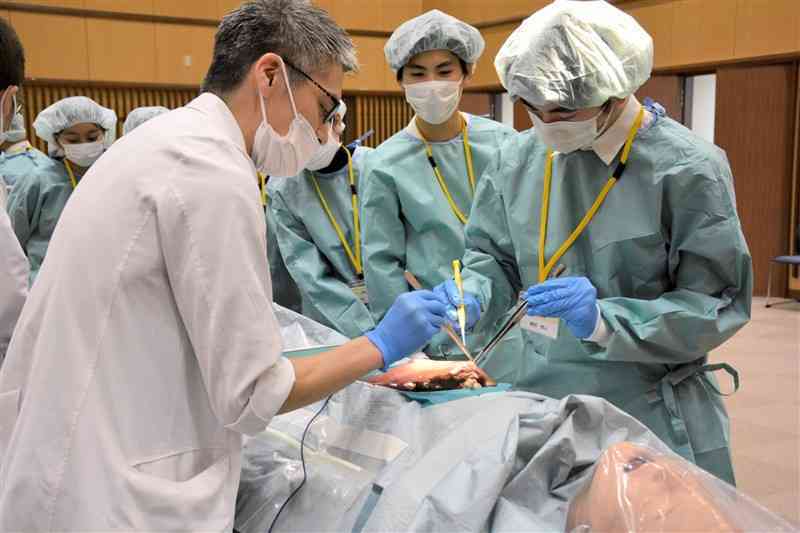 医師（左）に教わりながら、電気メスで豚の肝臓を切り取る生徒＝17日、熊本市東区