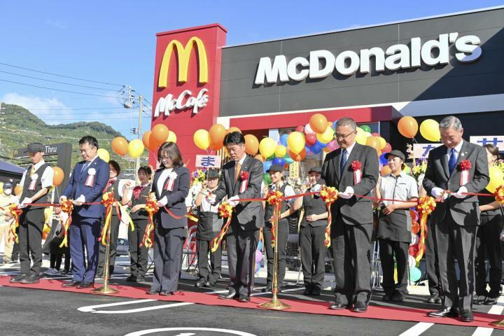 マクドナルド八幡浜店のオープンを記念し、はさみを入れる大石千枝社長（左から3番目）と大城一郎市長（右隣）ら＝11日午前、八幡浜市昭和通