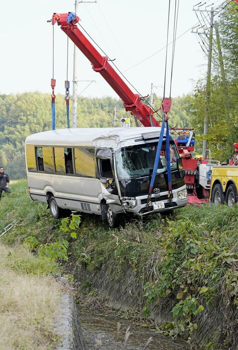 川に転落し、クレーンでつり上げられるマイクロバス＝22日午後0時35分、三重県桑名市