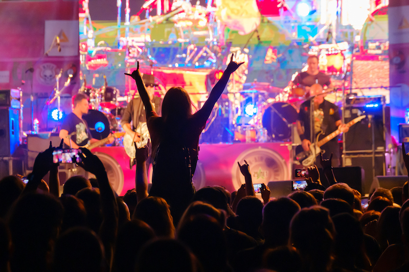 Fans at live rock music concert cheering musicians on stage, back view