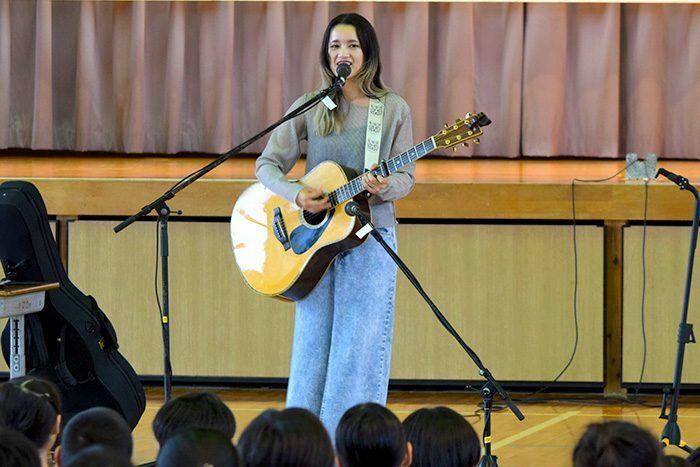 全校児童を前に即興で作った曲を披露するAnlyさん＝10月25日、伊江小学校体育館