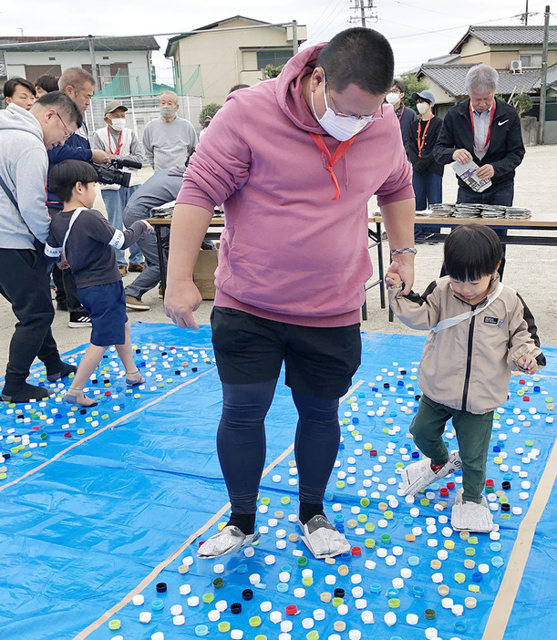 競争で新聞紙スリッパを試す親子連れ ＝大黒田町の花岡小で