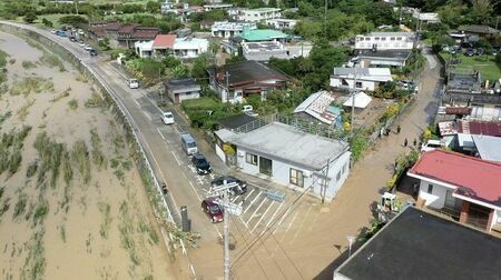 比地川（左）からあふれた水が集落まで流れ込み、道路や民家の敷地内が水浸しになった＝１０日午後０時５０分ごろ、沖縄県国頭村比地（ドローンで金城健太撮影）