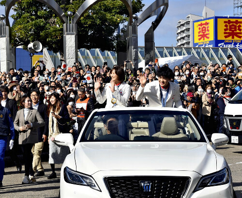 沿道の市民に手を振る角田選手（左）と安楽選手