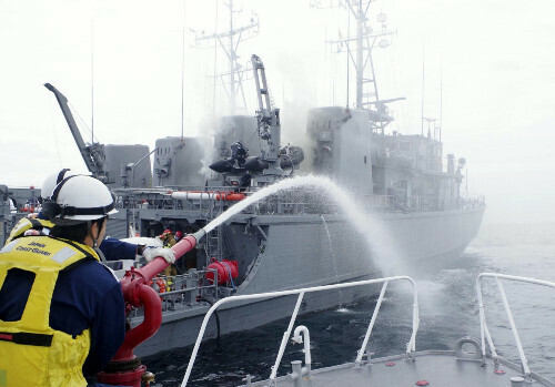 白煙を上げる掃海艇「うくしま」（奥）に放水する海上保安官（１０日）＝福岡海上保安部提供