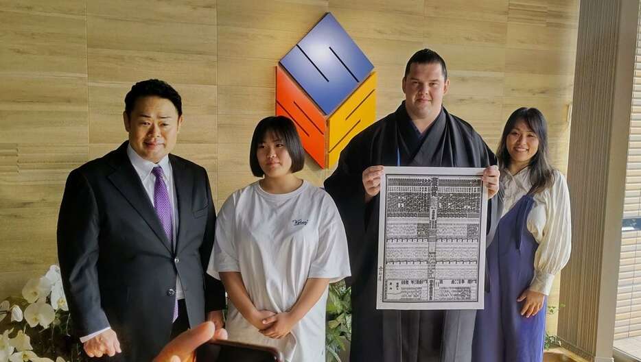 師匠の雷親方（左端）、おかみさんの垣添栄美さん（右端）、師匠の長女・星空（せいら）さん（左から2人目）に囲まれ、番付表を持つ新入幕の獅司＝10月28日、福岡市西区（宝田将志撮影）