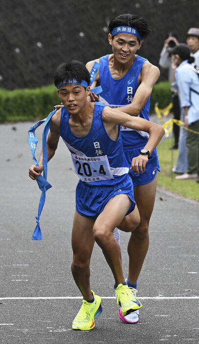 浜松日体の3区佐藤瑞城（右）からたすきを受け走り出す4区古井海成＝小笠山総合運動公園