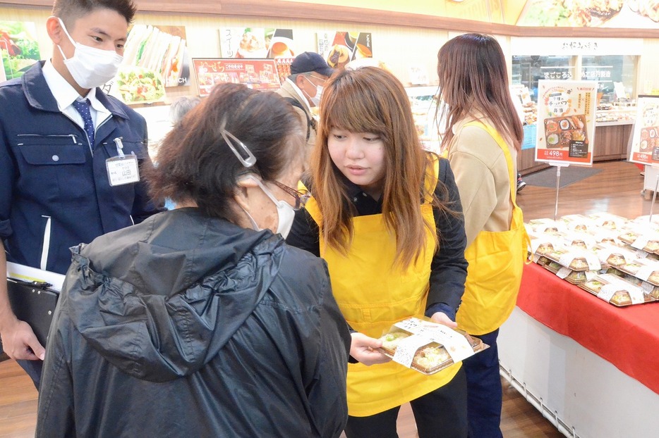 来店者に開発した弁当を薦める学生（アルク琴芝店で）