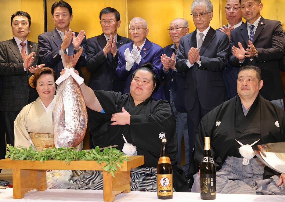 祝勝会場で鯛を持ち上げる琴桜（中、右は佐渡ヶ嶽親方、左は母でおかみの真千子さん）（カメラ・豊田　秀一）