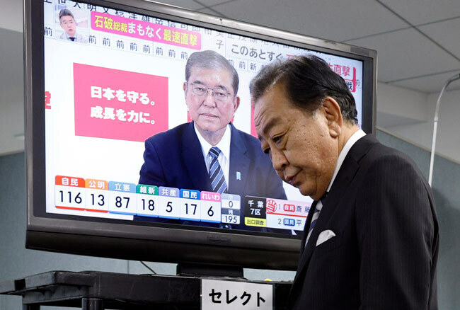 衆院選投開票日、石破茂首相を映すテレビ画面の前を通り過ぎる立憲民主党の野田佳彦代表＝2024年10月27日、東京・永田町