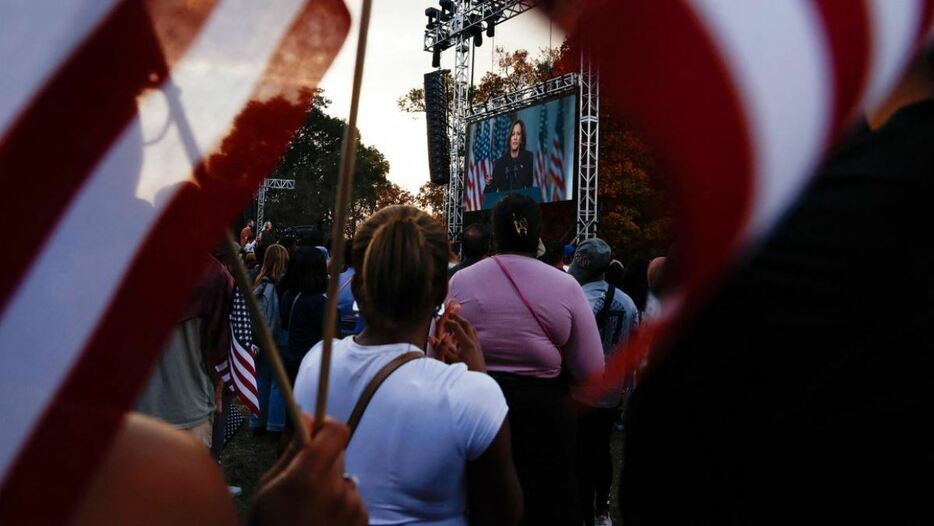 米大統領選での敗北を認める演説を行うカマラ・ハリス氏が映し出されたスクリーンを眺める支持者ら＝６日、米首都ワシントン