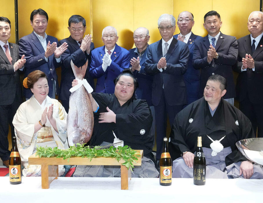 初優勝を飾った琴桜（中央）は千秋楽パーティー会場で関係者の祝福を受けながらお祝いの鯛を持ち上げる。右は父であり師匠の佐渡ケ嶽親方、左は母でおかみの真千子さん（撮影・小沢裕）