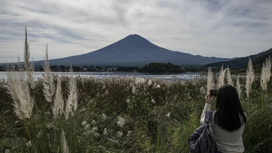 富士河口湖町で冠雪していない黒い富士山を写真に撮る女性（10月31日、AFP=時事）