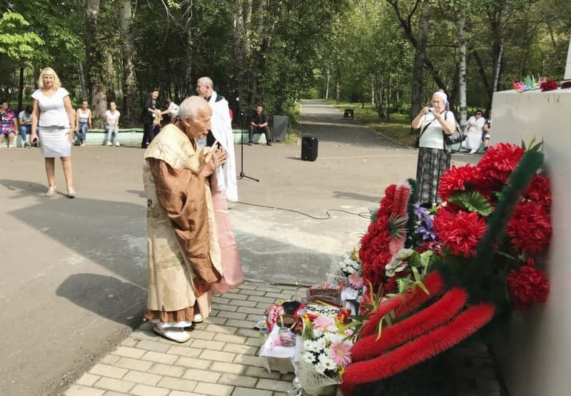 ロシア極東アムール州のイワノフカにある「哀悼の碑」の前で、手を合わせる横山周導さん（中央）＝２０１８年８月（共同）