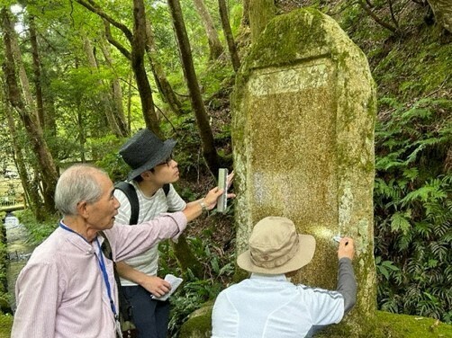 滋賀県醒井養鱒場が開始した放流事業で犠牲になった小アユを供養する「生き物供養碑」を調査するフィールドリポーターら＝滋賀県立琵琶湖博物館提供