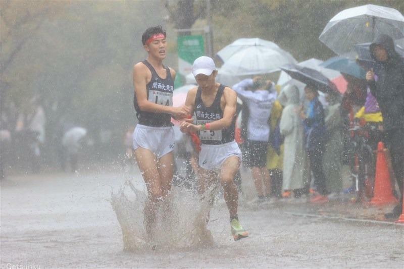 激しい雨の中でタスキリレーをする男子選手