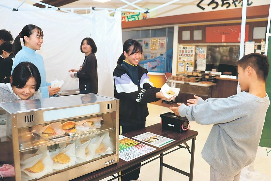 買い物客にライスバーガーを手渡す中田中の生徒（右から２人目）