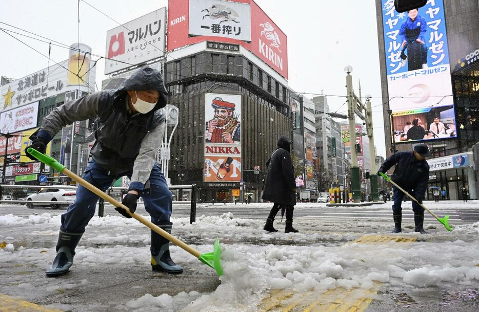 札幌市の繁華街・ススキノで雪かきをする人たち＝7日午前