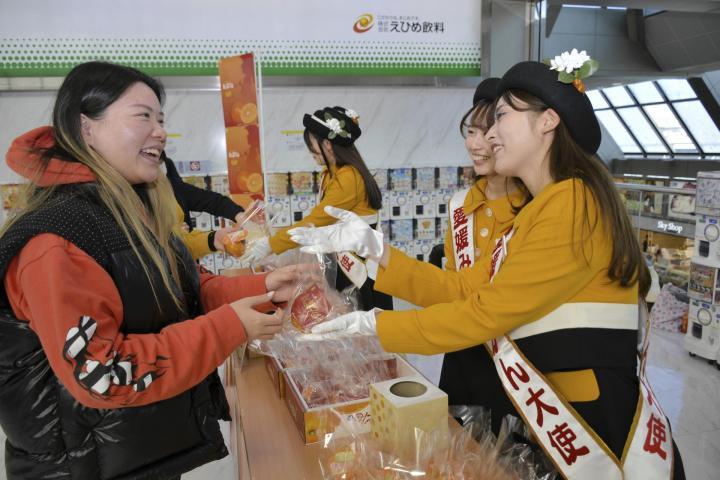 愛媛みかん大使（右）から紅まどんなを受け取る空港利用者＝23日午前、松山市南吉田町