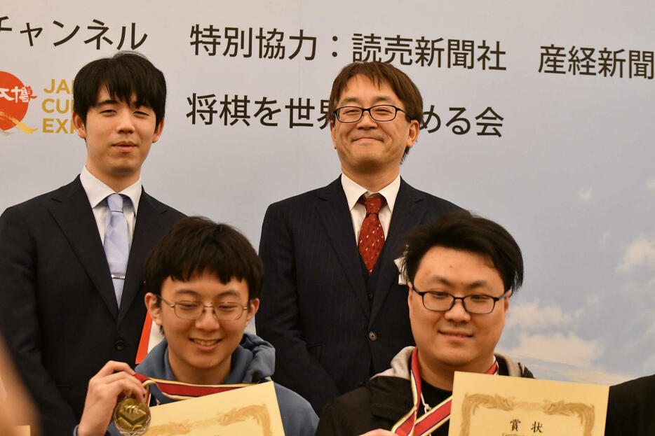 藤井聡太7冠（後列左）と日本将棋連盟会長の羽生善治九段（同右）は国際将棋トーナメントの上位入賞者との撮影に応じる