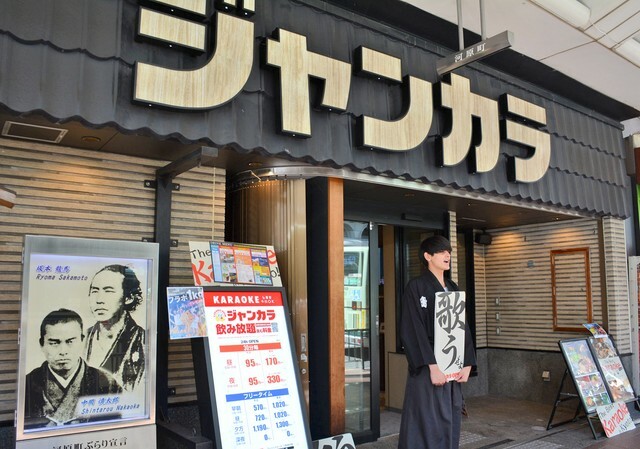 「歌うぜよ」と書いたボードを持って呼びかけるジャンカラ京都河原町近江屋店の店員（京都市中京区河原町蛸薬師下ル）