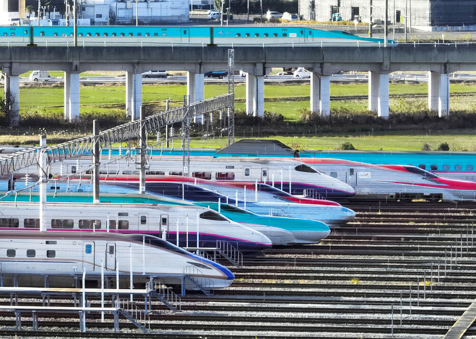 新幹線総合車両センターに鼻先をそろえて並ぶさまざまな車両。近くの高架線路を東北新幹線が風のように走り抜けていった