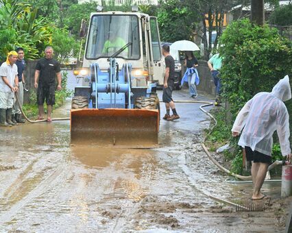 川から道路へと押し寄せた泥を片付ける住民ら＝１０日午前１１時３３分、国頭村比地（竹尾智勇撮影）