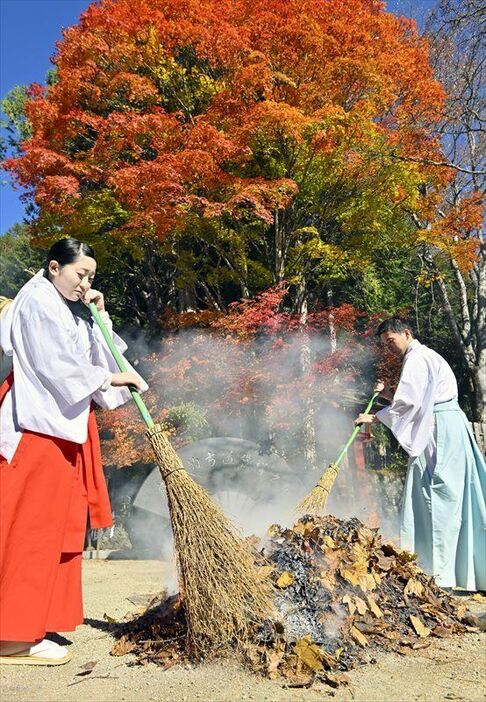 紅葉が残る木々の前で落ち葉たきをする神職と八乙女＝７日午前10時５分、日光市中宮祠