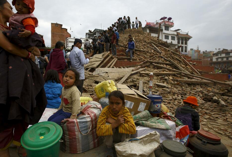 倒壊した建物の前で座る子どもら(ロイター/アフロ)
