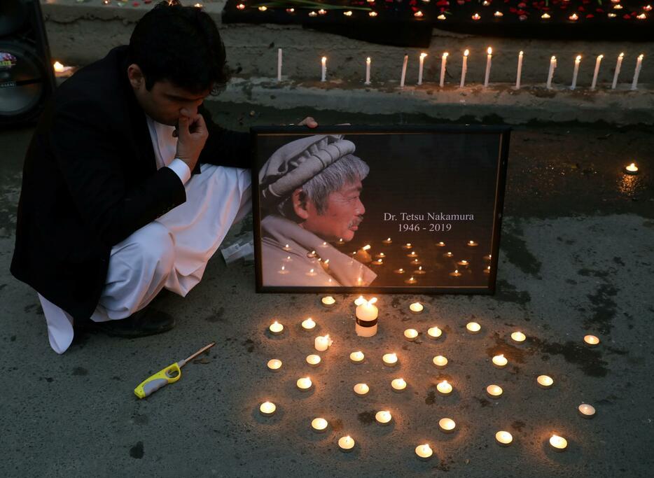 中村哲さんの写真の前に蝋燭（ろうそく）を並べた男性。2019年12月5日、アフガニスタンの首都カブールにて（写真：ロイター/アフロ）