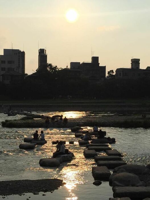 [写真]夕陽色に染まった鴨川。足を川に入れて涼むカップルらの姿が多くみられる＝30日午後5時40分ごろ、京都市左京区で