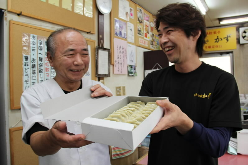 [写真]持ち帰りのギョウザを手に笑う「餃子の店かず」の村瀬一夫さん(左)、光孝さん親子