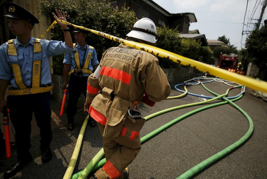 規制線をくぐり抜ける消防士。事故では3人が死亡＝2015年7月26日（写真：ロイター/アフロ）