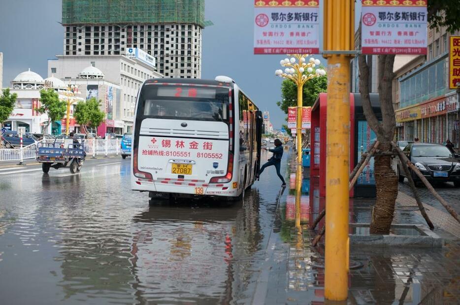 水たまりの中でバスに乗る女性。少しの量の雨で下水が逆流し、道路が水びたしになってしまった＝シリンゴル盟・シリンホト市（2014年6月撮影）