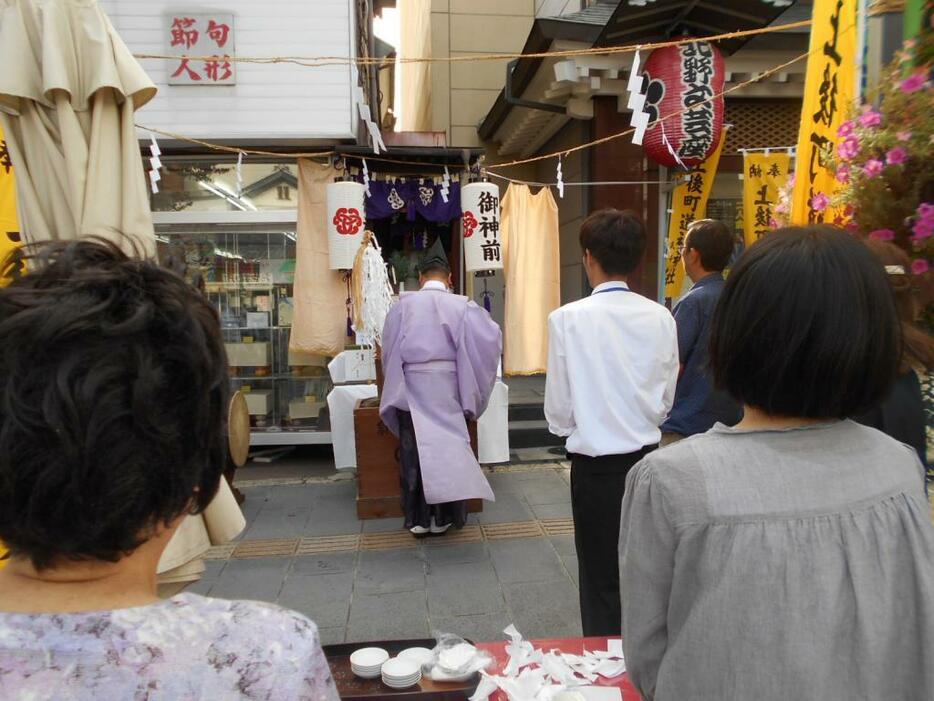 [写真]ビルと商店のすき間に古くからある道祖神で宵宮祭り