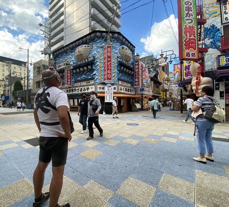 [写真]巨大ふぐ看板がなくなり寂しいが、看板跡を見上げながら「今は耐えしのぐしかない」と語る國領翔太さん