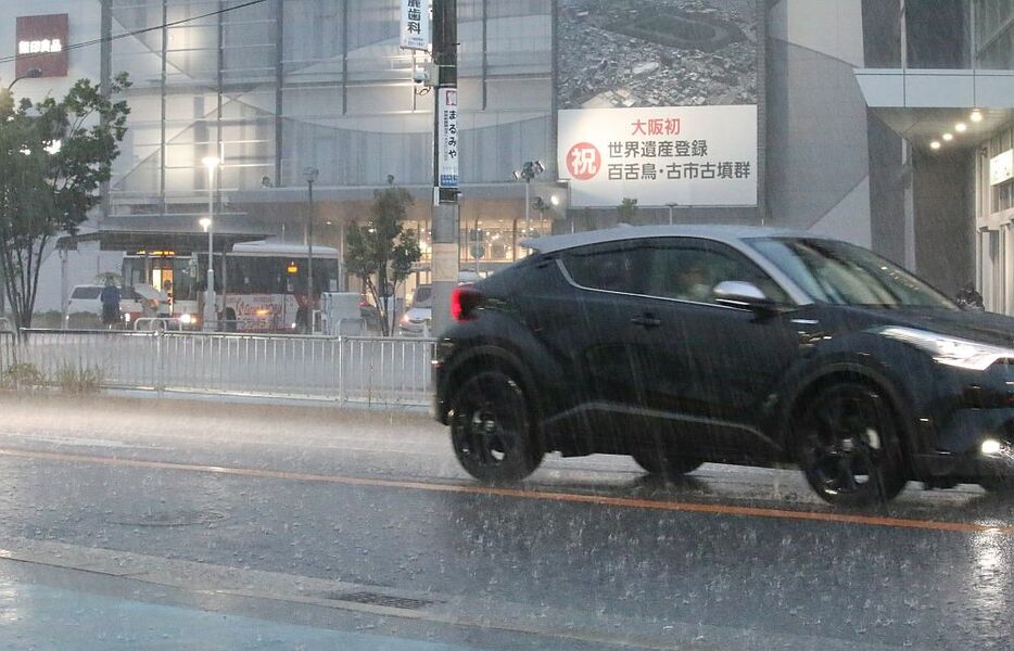 [写真]突然、路上を激しく打ちつける猛烈な雨が降り、近くのショッピングセンター入り口で雨やどりする人の姿が多くみられた＝5日午後6時5分ごろ、大阪府堺市北区で