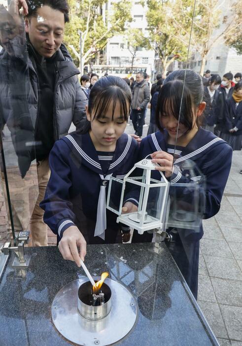 「1.17希望の灯り」の分灯が始まり、ろうそくに火を移す中学生＝7日午後、神戸市中央区の東遊園地