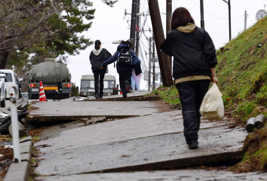 22日で能登半島地震発生から3週間の石川県輪島市で、自宅から持ち出した日用品を手に高台の避難所へ向かう親子。2次避難先となるアパートは金沢市内に確保したという。母親（手前）は「娘たちもみんなと同じ学校に転校できたらよかったけど。ばらばらになっていくので心配」と話した＝21日午前