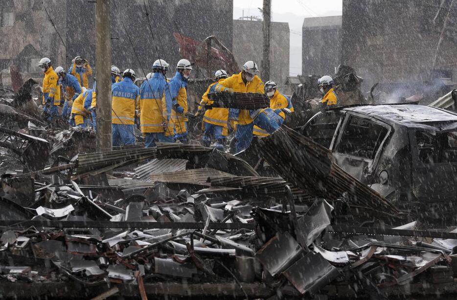 大雨が降る中、大規模火災があった「輪島朝市」付近でがれきを撤去する警察官ら＝6日午前10時、石川県輪島市