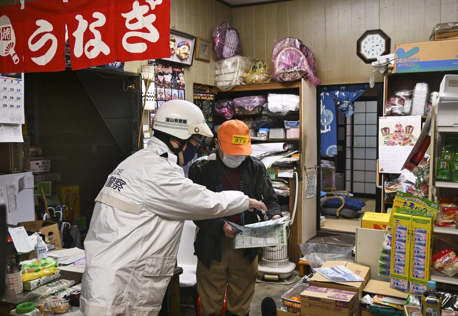 地震で被災した富山県高岡市で、窃盗や住居侵入、悪質商法などへの注意を呼びかける警察官（左）＝6日午後