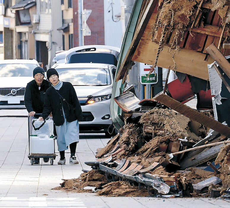 倒壊した店舗の横を通って支援物資を運ぶ被災住民＝４日午前１１時４０分、七尾市一本杉町