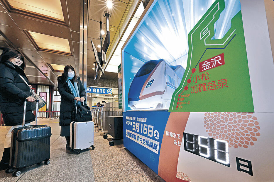 石川県内全線開業まで５０日のカウントボードに見入る利用客＝２６日午前１１時半、ＪＲ金沢駅
